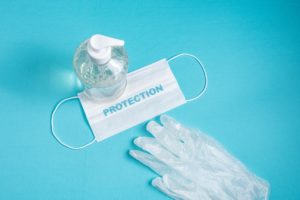 Container with alcohol gel, gloves and surgical mask on the light blue background